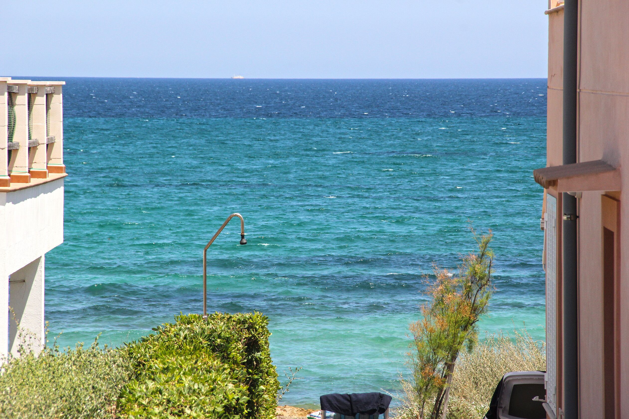 Vista al mar desde un balcón con barandilla de metal, un pequeño jardín y un coche estacionado cerca.