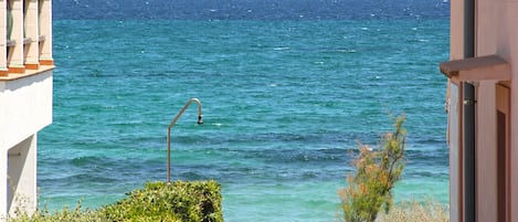 Vista al mar desde un balcón con barandilla de metal, un pequeño jardín y un coche estacionado cerca.