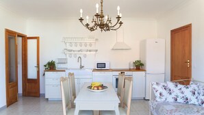 Een compacte keuken met een eettafel, stoelen, een kroonluchter en een koelkast.