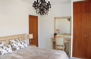 A bedroom with a bed, a desk, a chair, a mirror, and a wardrobe.