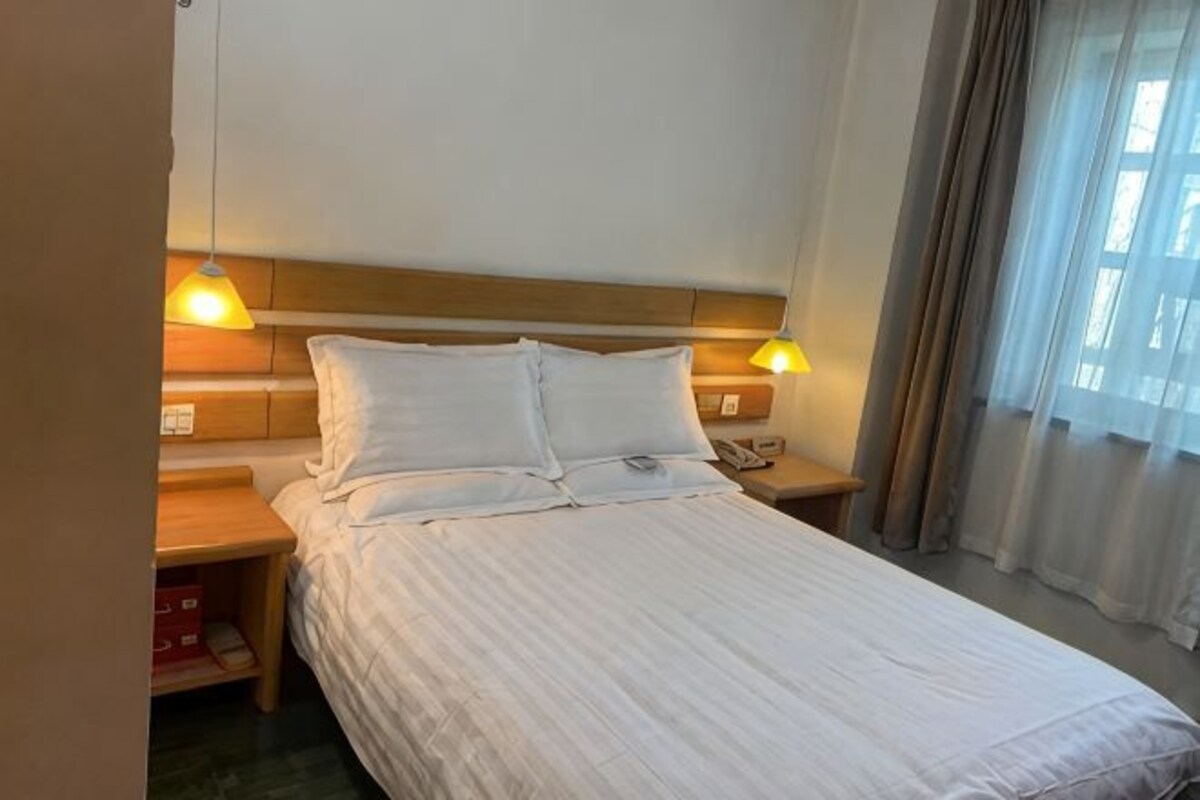 Una camera d'albergo con un letto, abat-jour, comodino e una finestra con tende.