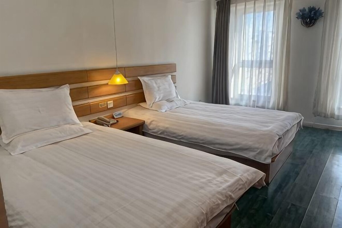 Ett hotellrum med två sängar, en sänggavel i trä, ett nattduksbord med en lampa och ett fönster med gardiner.