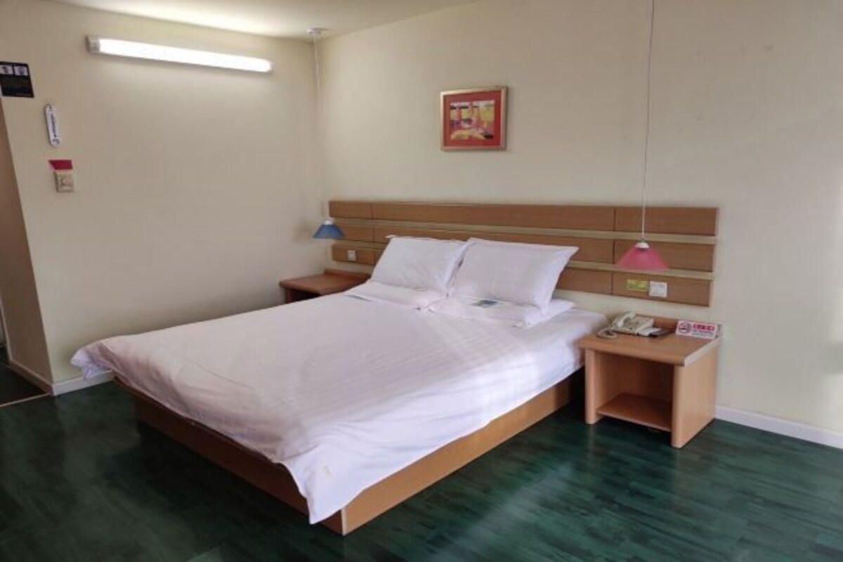 Un letto ben rifatto con lenzuola bianche, una testiera in legno e un comodino con una lampada e un telefono.