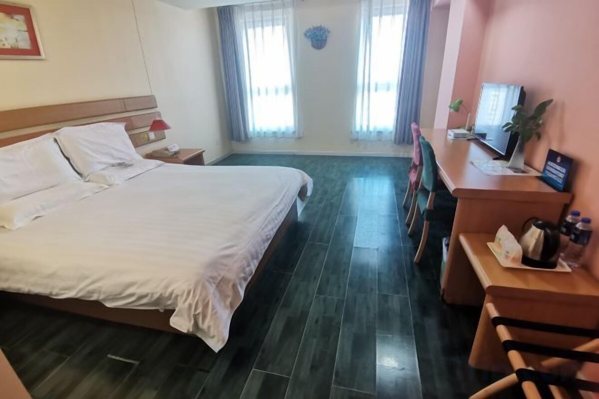 Habitación de hotel con cama, escritorio, silla, televisor y ventana con cortinas.