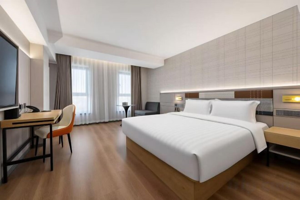 A hotel room with a large bed, a desk, a chair, and a television.