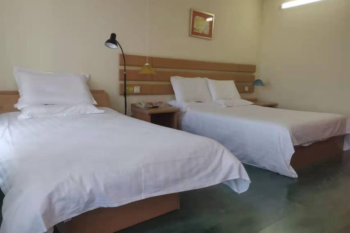 Ett hotellrum med två separata sängar, ett nattduksbord med en lampa och en inramad tavla på väggen.