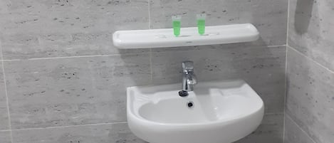 Une salle de bain avec un lavabo sur colonne, un miroir et une étagère contenant des articles de toilette.