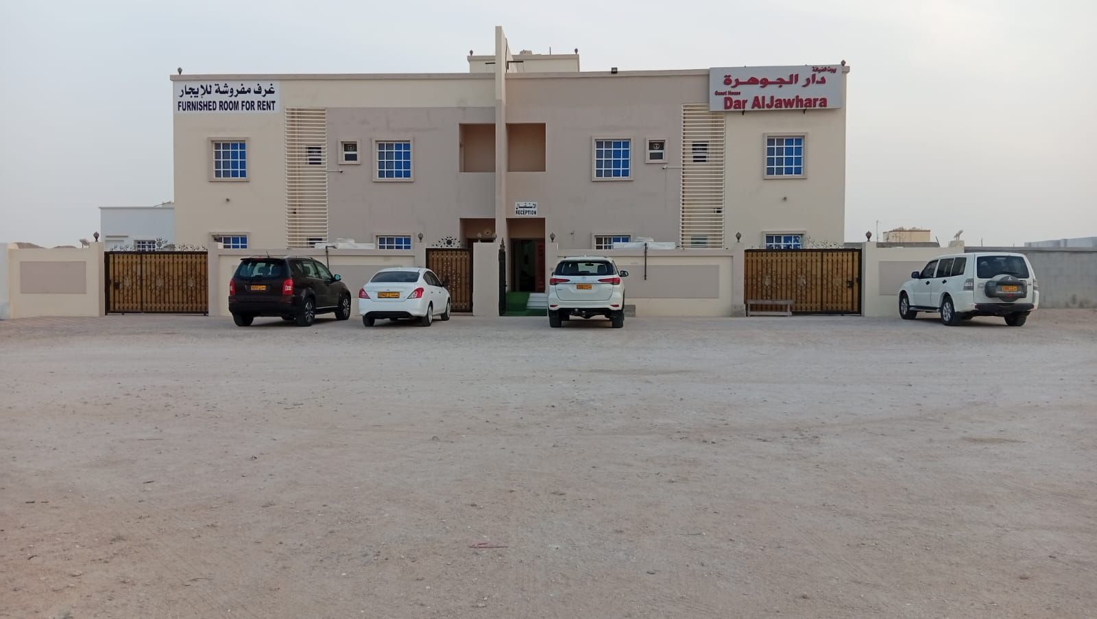 Un edificio con zona de recepción y varios coches estacionados en la parte delantera.