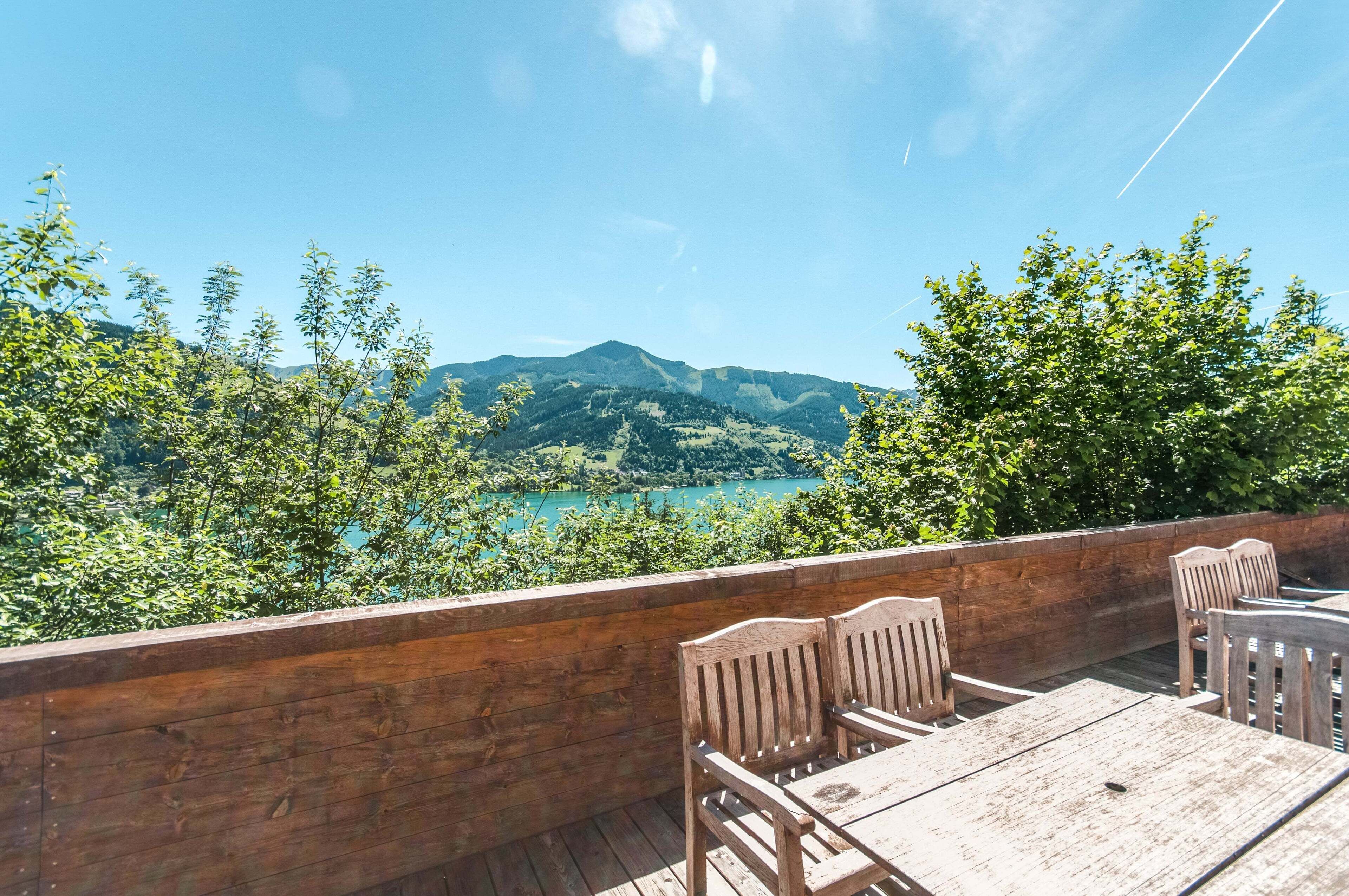 Een houten terras met een tafel en stoelen met uitzicht op een meer en bergen.
