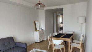 Een moderne woonkamer met een grijze bank, een witte salontafel, een eettafel met vier stoelen en een witte dressoir met spiegel.
