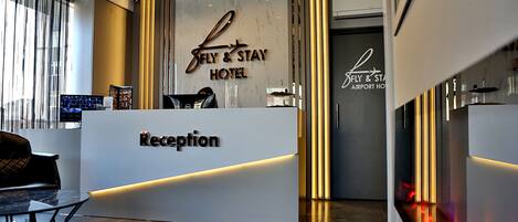 Un espace d’accueil au design moderne, comprenant un comptoir de réception portant l’inscription « Réception » et une enseigne au-dessus indiquant « FLY & STAY HOTEL ».