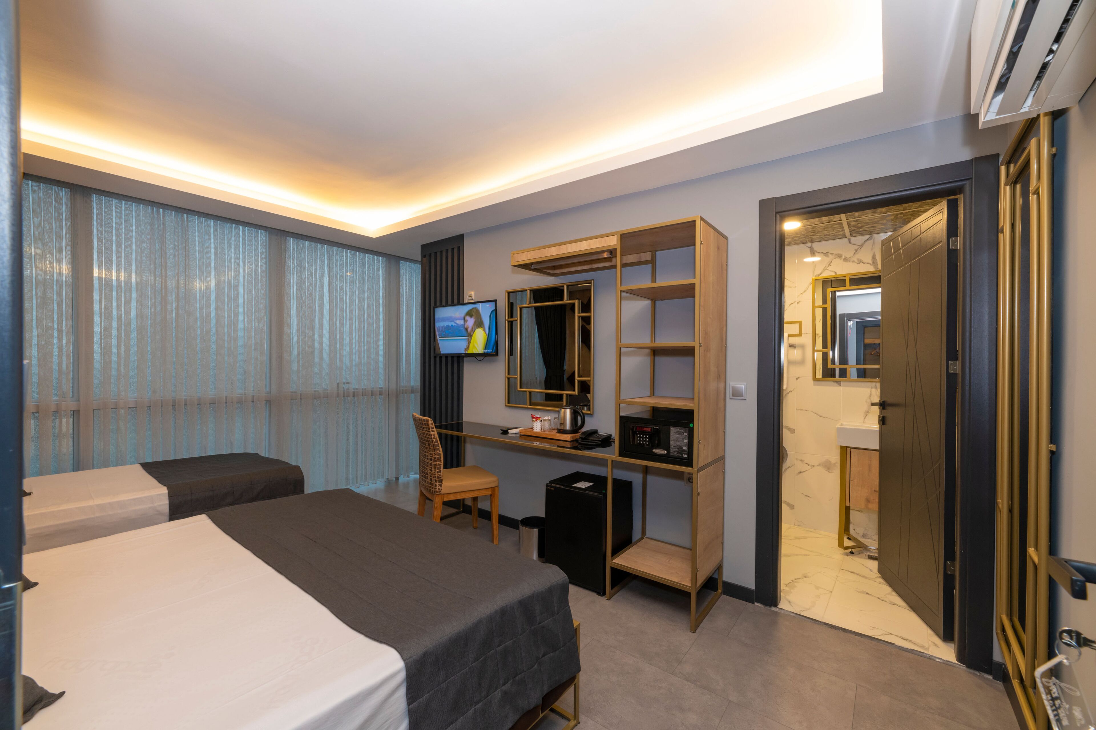 A hotel room with a bed, a desk with a computer, a TV, and a wardrobe.