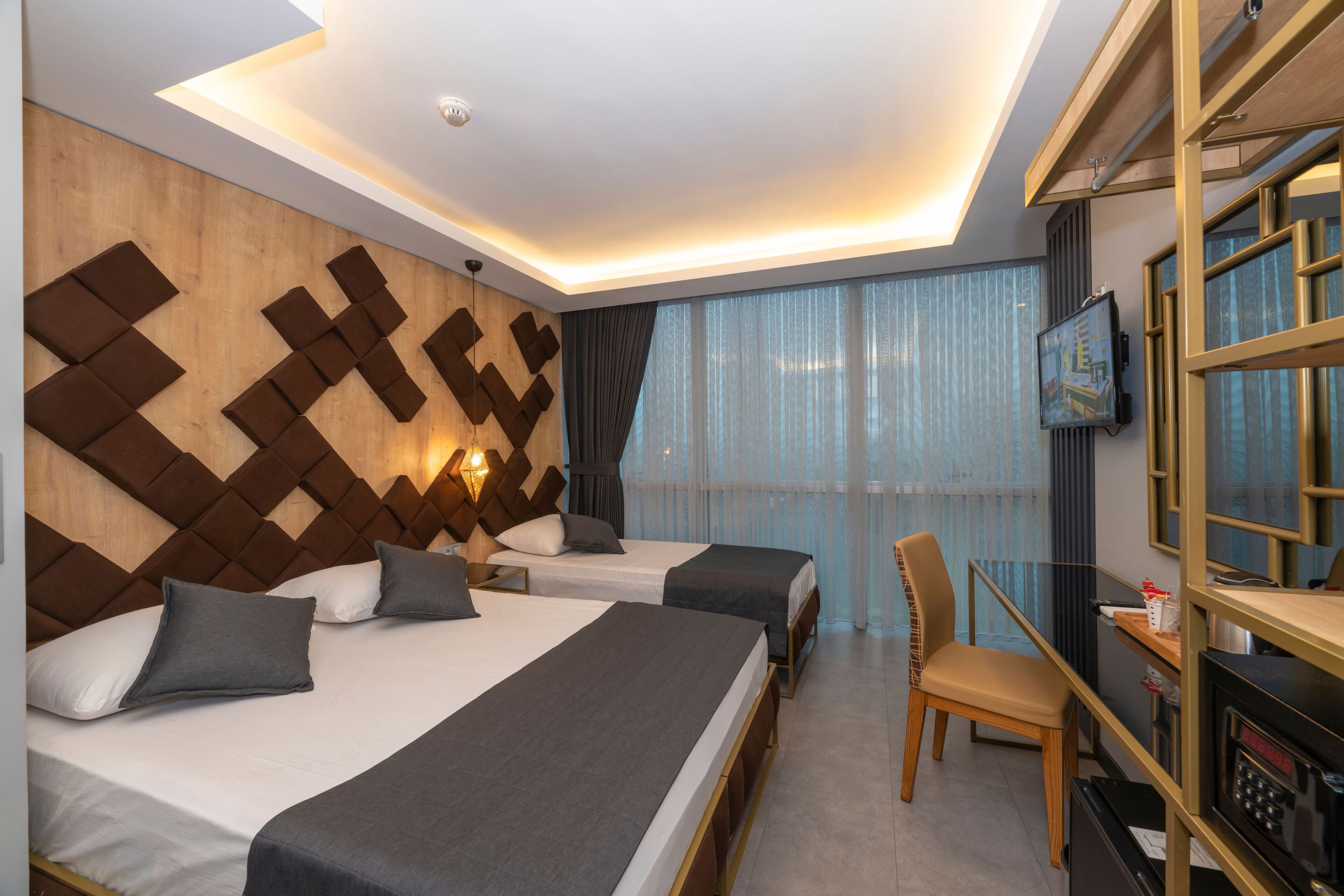 A hotel room with two beds, a desk with a chair, a television, and a large window with curtains.