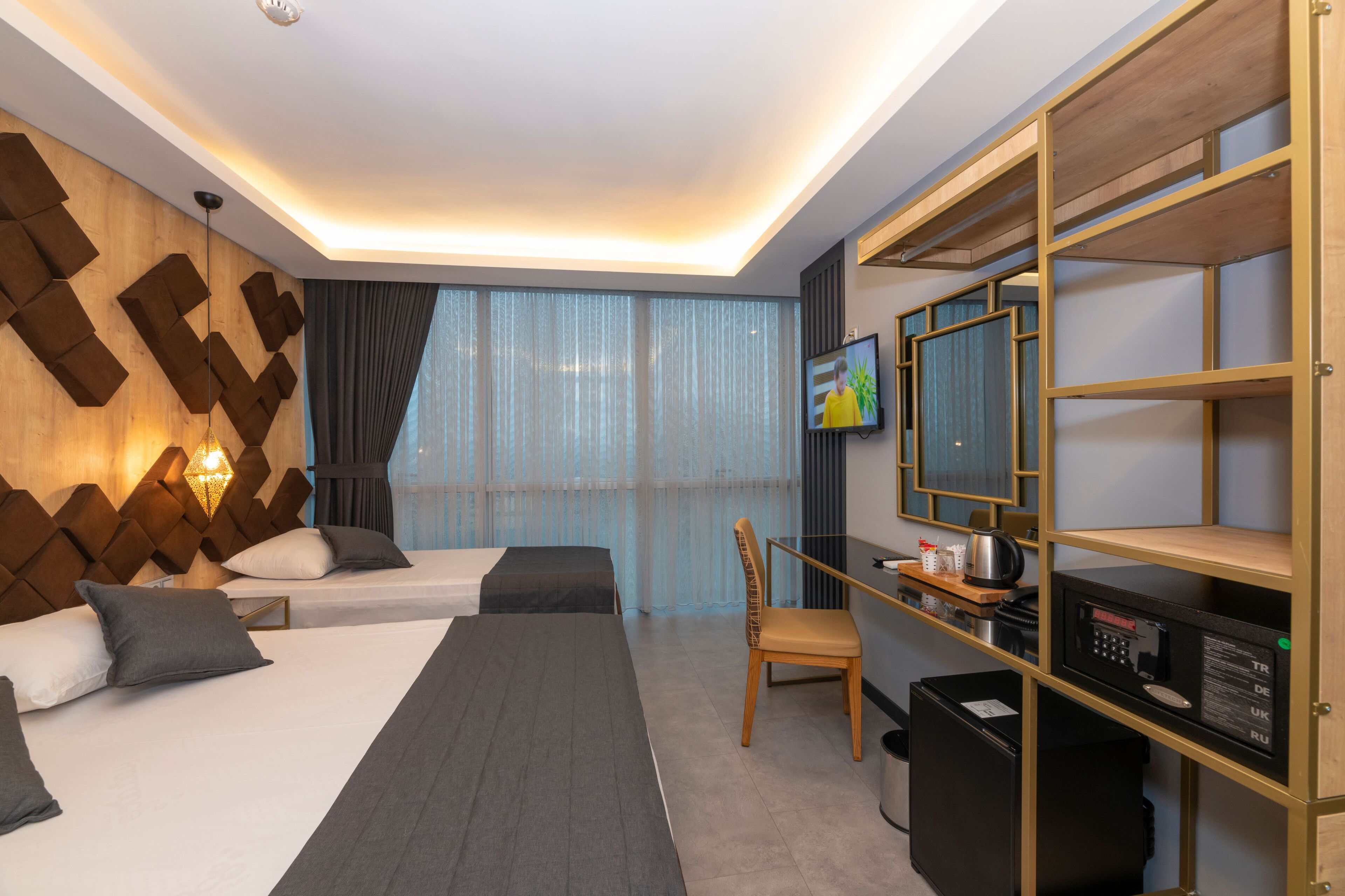 A hotel room with two beds, a desk with a computer, a TV, and a minibar.