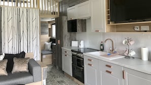 Een kleine keuken met witte kastjes, een inbouwoven en een grote, zwarte televisie boven de aanrecht.