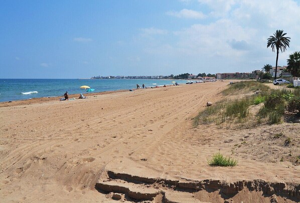 A wide sandy beach with a few umbrellas and people.