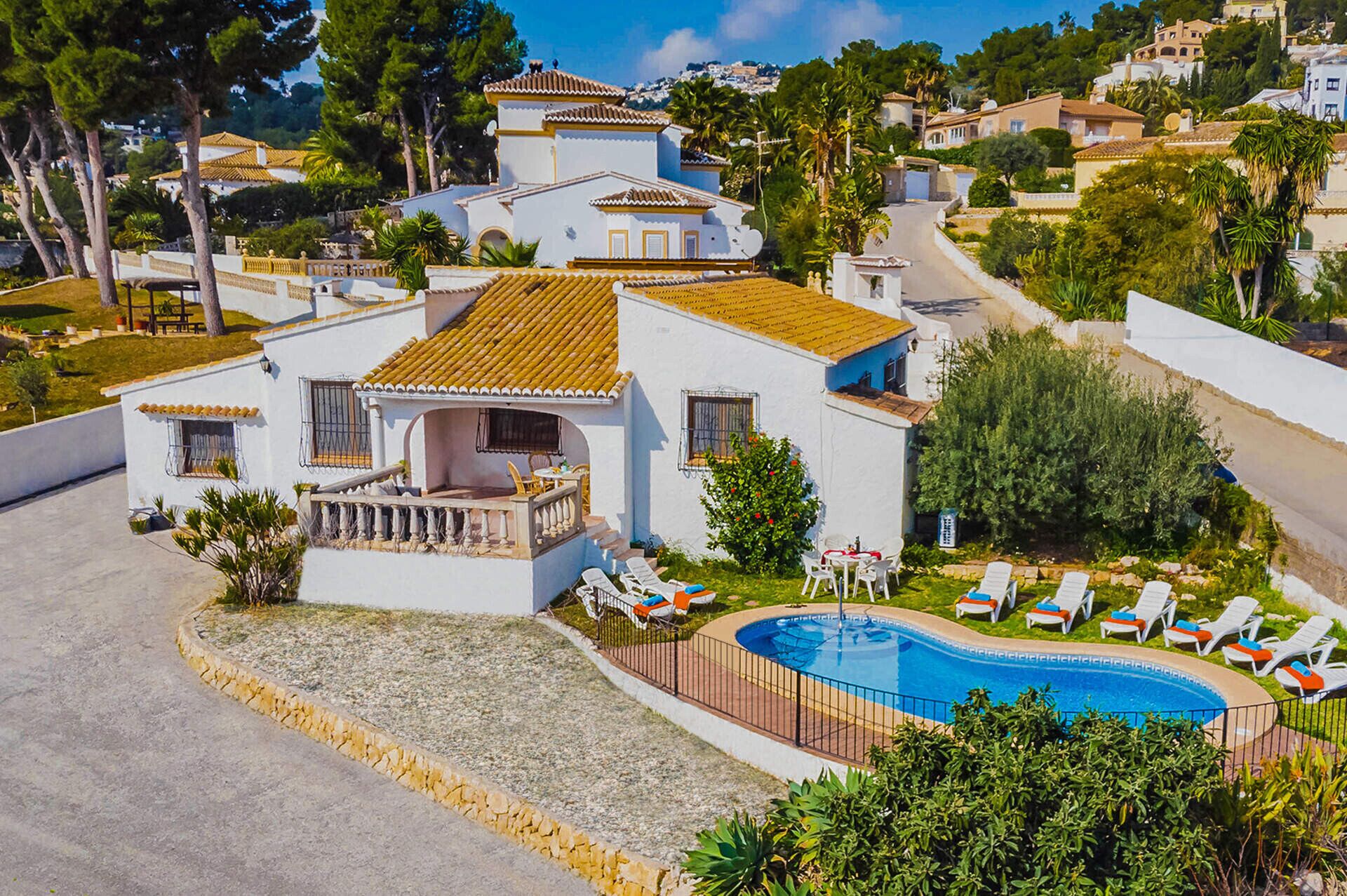 A white villa with a tiled roof, a swimming pool, and sun loungers.