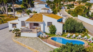 A white villa with a tiled roof, a swimming pool, and sun loungers.