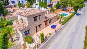 A stone house with a pool, a tennis court, and a street view.