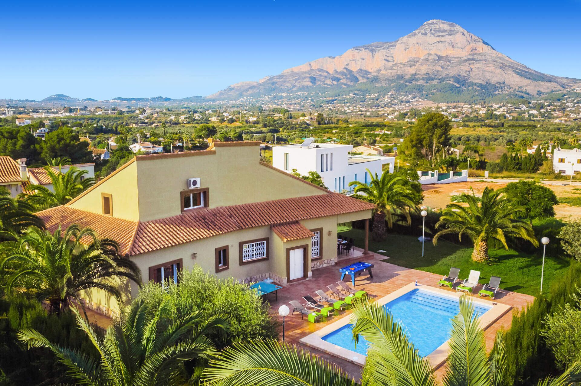 A residential area with a swimming pool, palm trees, and a mountain in the background.