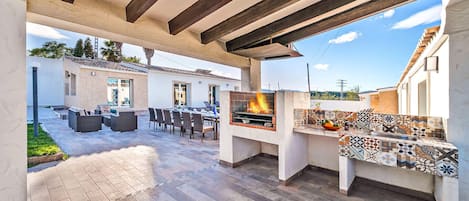 An outdoor patio with a built-in grill, seating area, and a tiled backsplash.