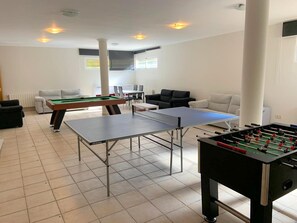 Uma sala de estar com mesa de pingue-pongue, mesa de futebol e mesa de bilhar.