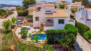 A Mediterranean-style villa with a swimming pool, multiple balconies, and lush greenery.