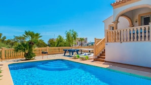 A swimming pool with a sun terrace, lounge chairs, and a staircase leading to a balcony.