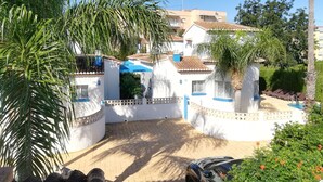 Un lotissement résidentiel fermé, doté d’une piscine, de palmiers et surplombant un ciel d’un bleu limpide.