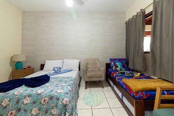 A bedroom with a bed, a chair, a sofa bed, a nightstand, and a lamp.
