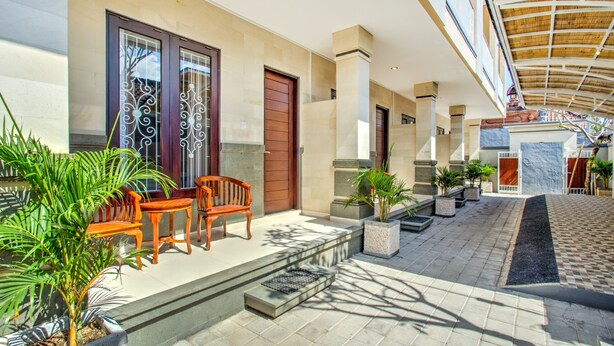 A spacious outdoor area with a wooden bench, potted plants, and a checkered floor. - OYO 3897 Fajar Guest House (Kerobokan)