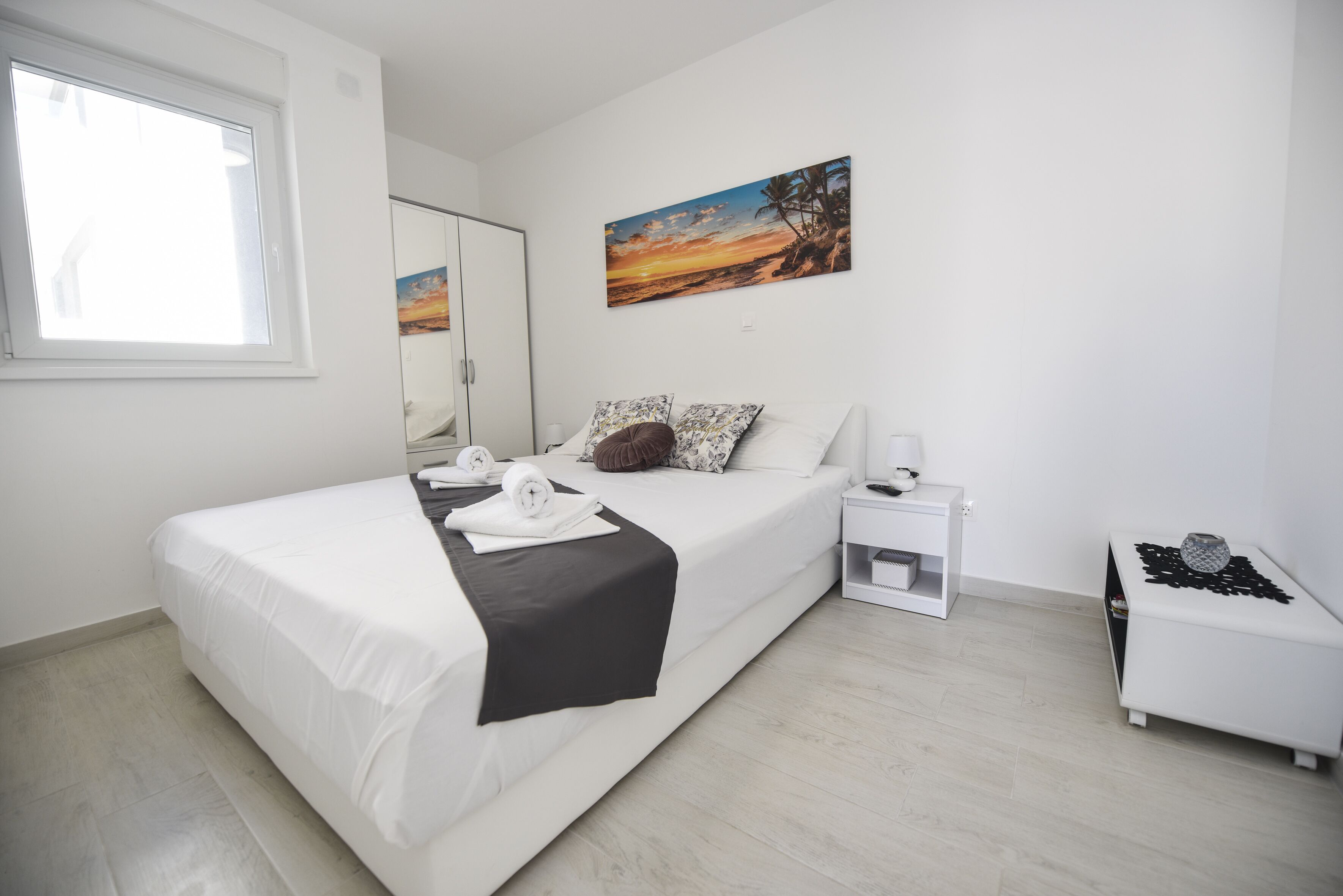 A modern bedroom with a bed, a nightstand, a bedside table, a window, and a painting on the wall.