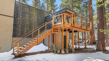 A wooden staircase leading to a deck with a metal railing, surrounded by trees and snow.