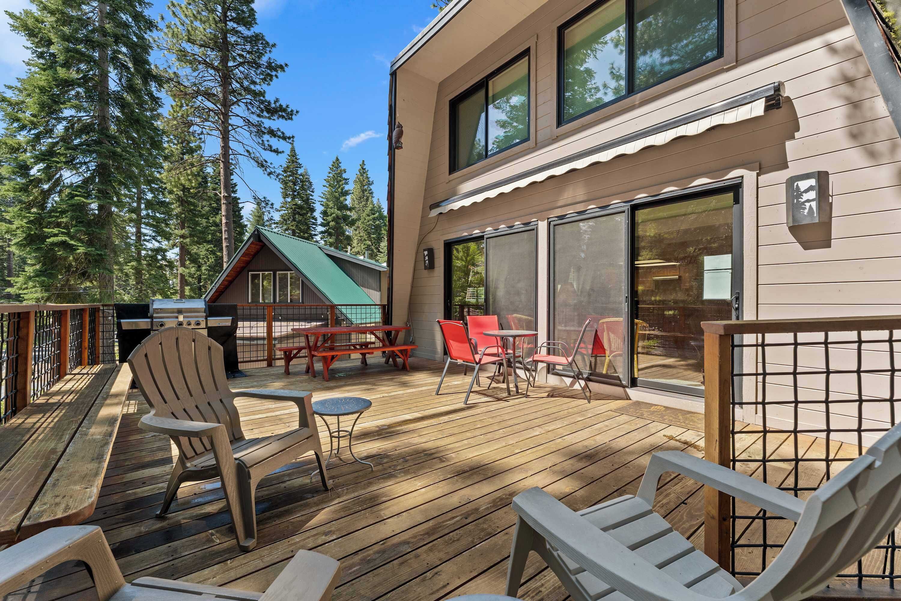 A wooden deck with outdoor furniture, a grill, and a building with large windows and a sliding door.