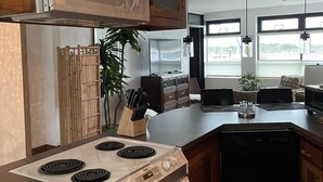Cozinha moderna com fogão, micro-ondas e máquina de lavar loiça. Possui um espaço de refeições com mesa e cadeiras.