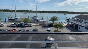 Uma marina com vários barcos atracados, área de estacionamento com carros e um edifício com mesas ao ar livre.