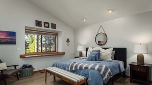 A bedroom with a bed, bench, bedside tables, a window, and a view of trees. - Lake Views, Hot Tub, Across from Beach, Garage "Sandy Shores Villa" (Tahoe Vista)