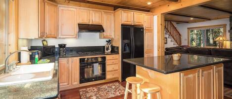 A kitchen with wooden cabinets, a black refrigerator, a stove, and a large island with stools.