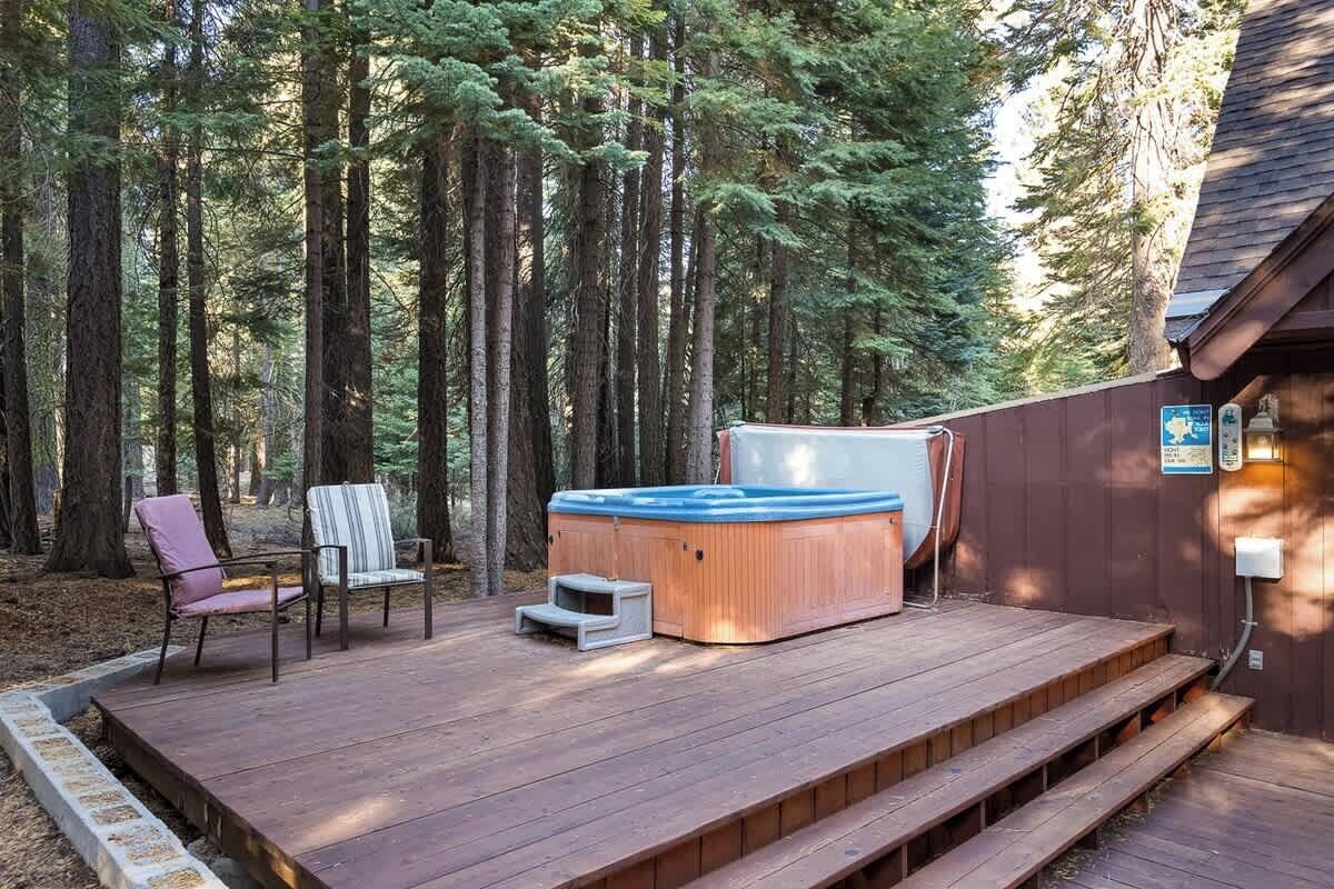 Een houten terras met een jacuzzi, twee stoelen en een kleine trap naar een gebouw.