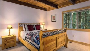 A wooden bed with a headboard, two bedside tables with lamps, a window with a view of trees, and a framed picture on the wall. - Hot Tub with Forested Views plus Garage in Quiet Neighborhood (Tahoma)