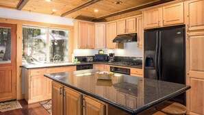 A kitchen with wooden cabinets, a black refrigerator, and a large island with stools. - Hot Tub with Forested Views plus Garage in Quiet Neighborhood (Tahoma)