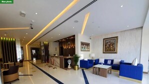 A modern hotel lobby with a reception desk, blue sofas, a coffee table, and a reception area with a wooden panel wall. - Skylark Hotel Apartments (Dubai)
