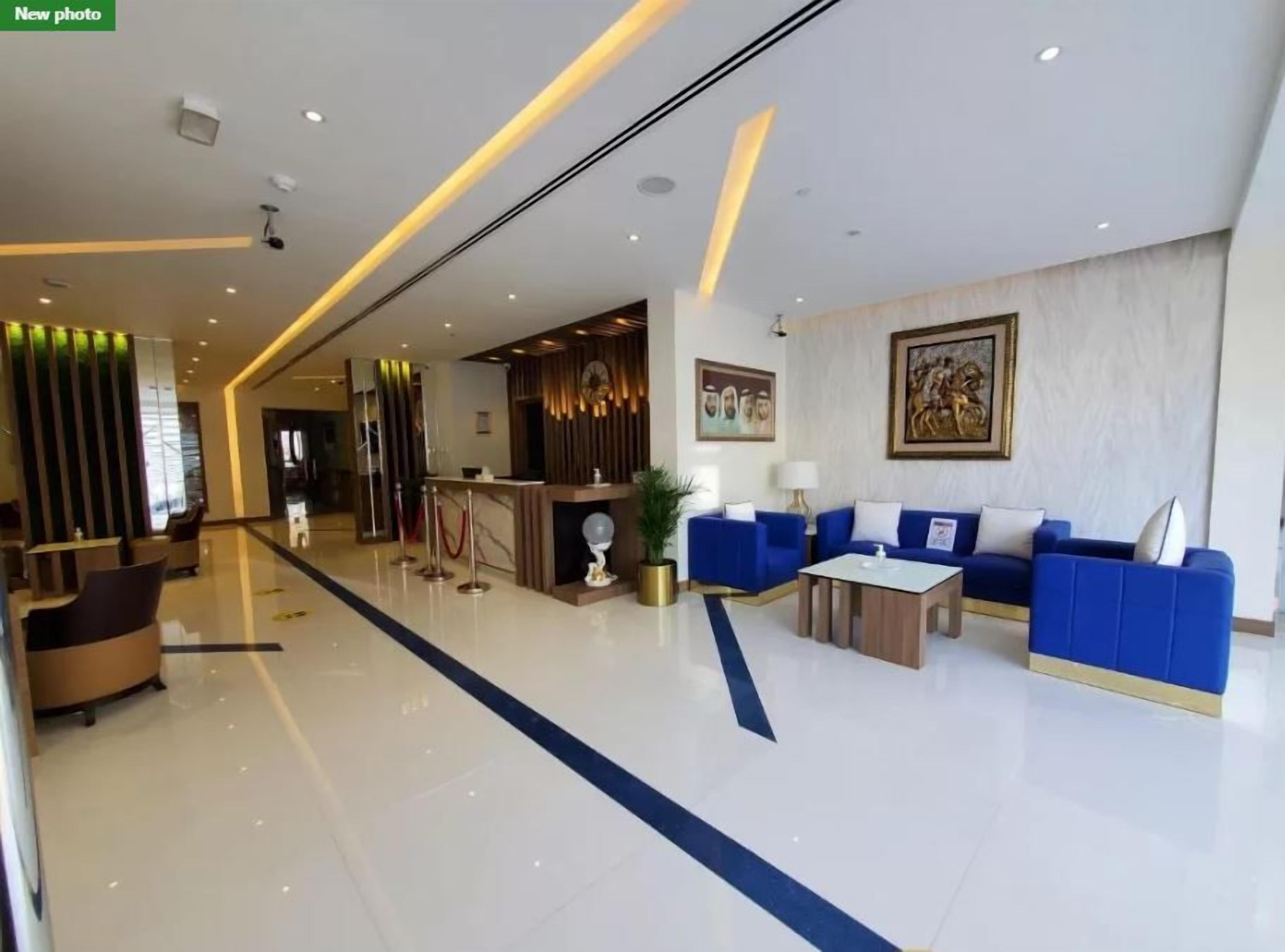 A modern hotel lobby with a reception desk, blue sofas, a coffee table, and a reception area with a wooden panel wall.