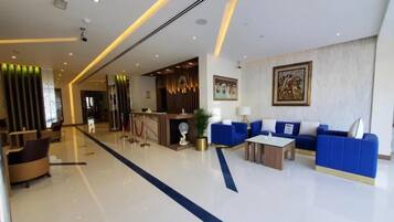 Um hall de hotel moderno com um balcão de recepção, sofás azuis, uma mesa de centro e uma área de atendimento com painel de parede de madeira.