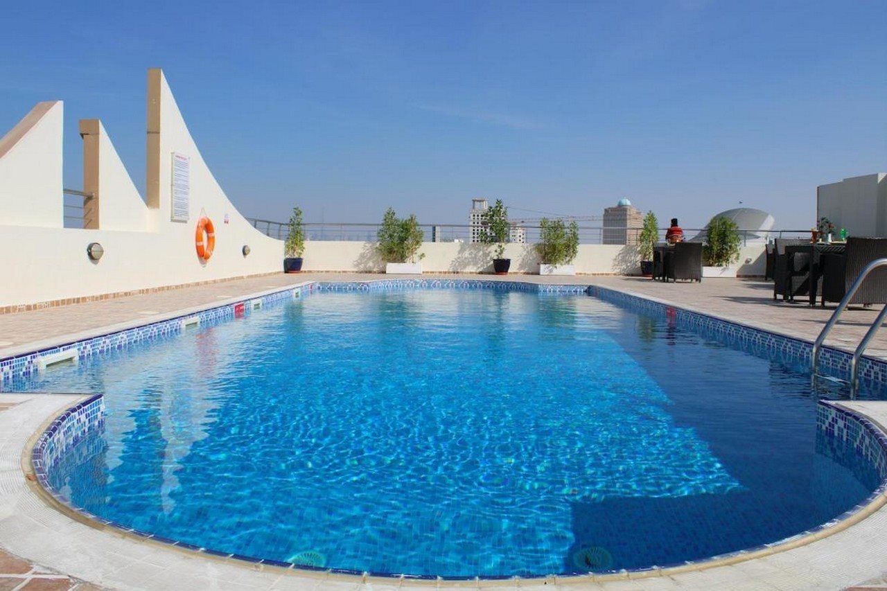 A rooftop swimming pool with a clear blue water, surrounded by potted plants, and a view of the city skyline.