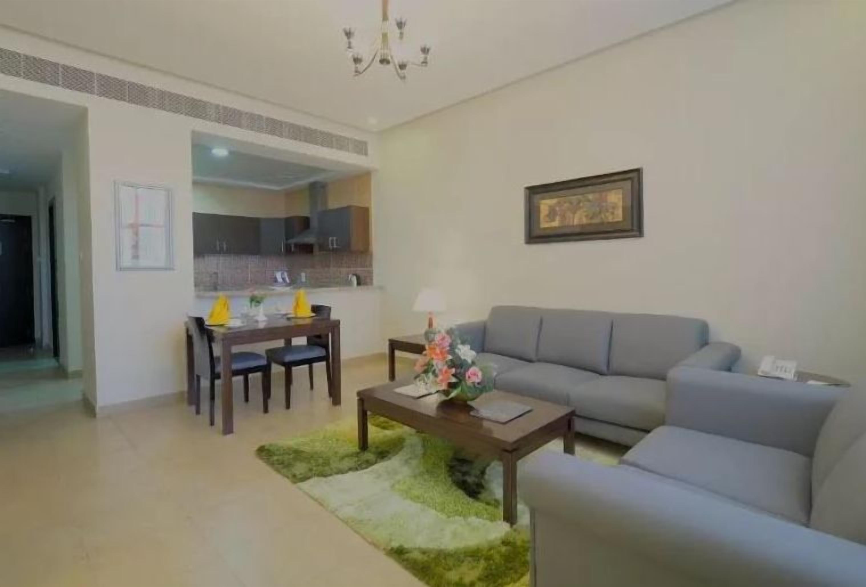 A living room with a sofa, a dining table with chairs, a coffee table with flowers, and a kitchen in the background.