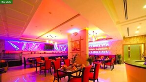 A restaurant with red chairs, a bar area, and a TV screen on the wall. - Skylark Hotel Apartments (Dubai)