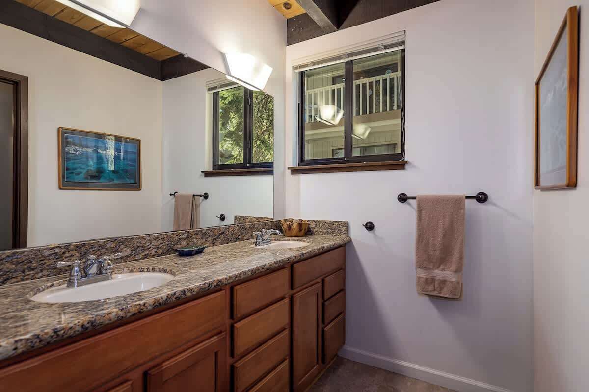 A bathroom with a granite countertop, two sinks, wooden cabinets, a towel rack, and a framed picture on the wall.