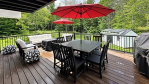 A wooden deck with a table and chairs, two red umbrellas, and a grill.
