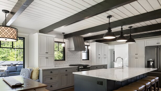 A modern kitchen with white cabinets, a large island with stools, a built-in oven, and a coffee station.
